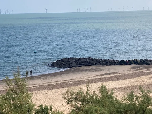 Clacton on Sea beach with a rocky groyne and offshore wind turbines on the horizon